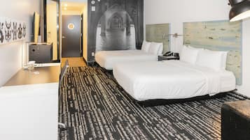 A hotel room with two beds, a desk, a mirror, a wall art of an archway, and a patterned carpet.