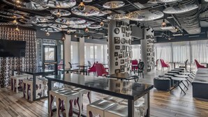 A modern interior with a central bar area, seating arrangements, and a ceiling adorned with circular patterns. - Lorenzo Hotel Dallas, Tapestry Collection by Hilton (Dallas)
