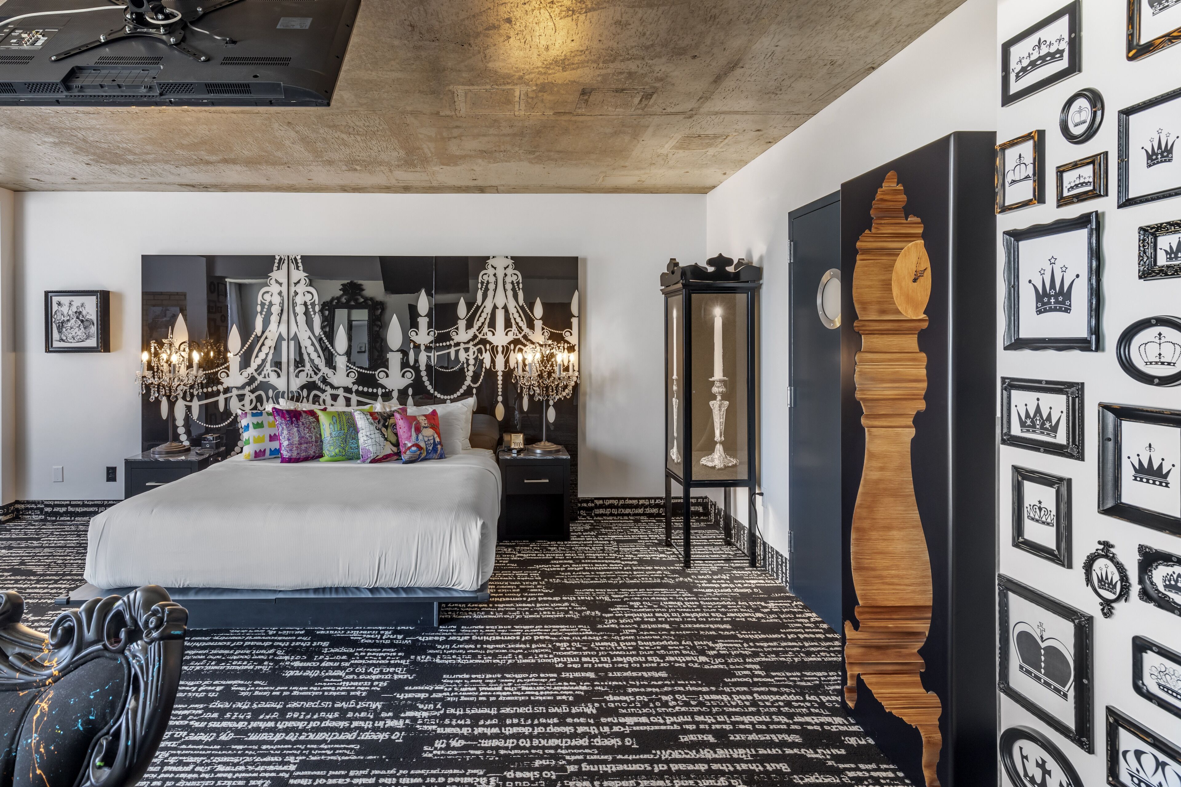 A bedroom with a large bed, a chandelier, a wooden clock, and a wall decorated with framed pictures.