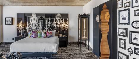 A bedroom with a large bed, a chandelier, a wooden clock, and a wall decorated with framed pictures.