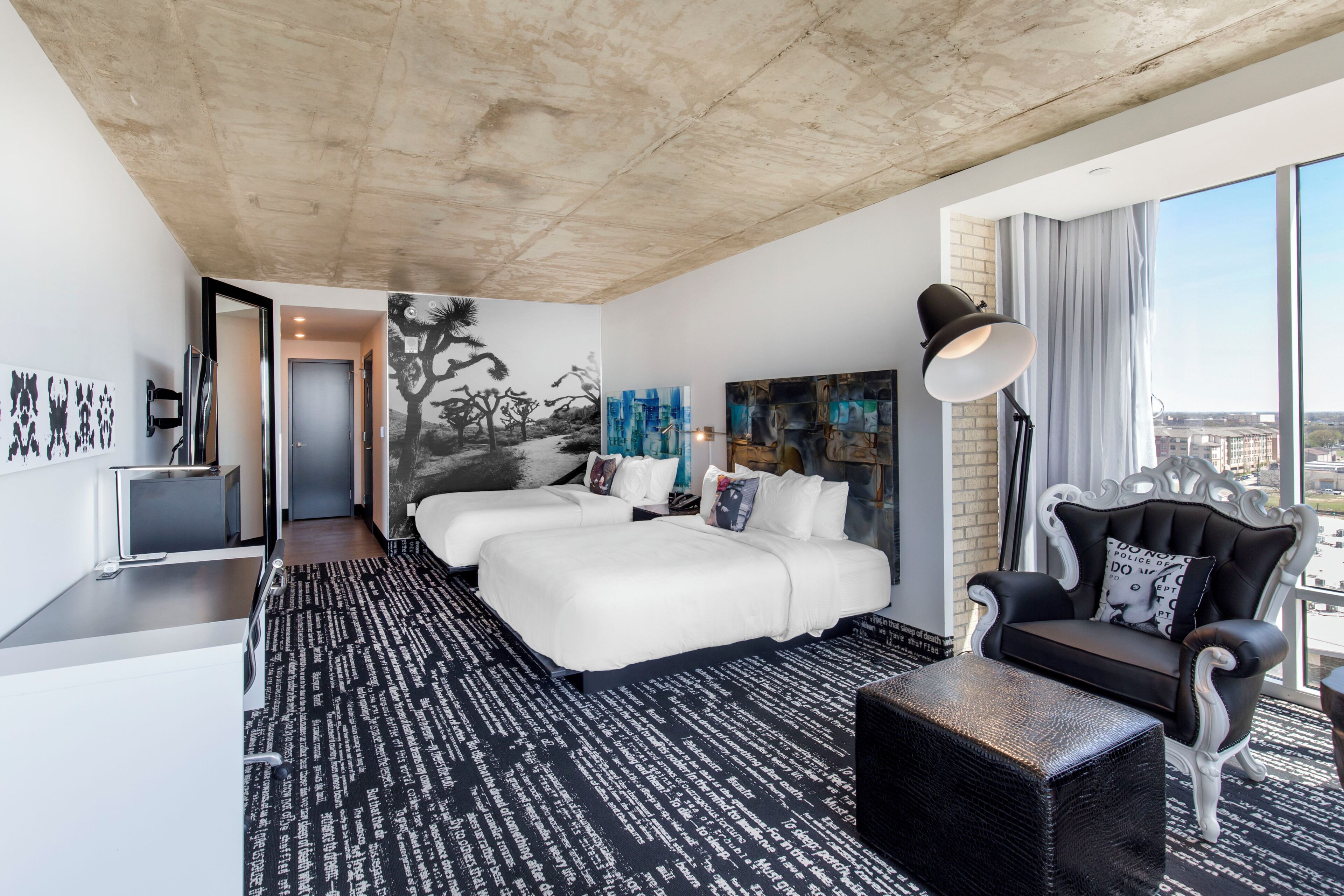 A modern hotel room with a large bed, a seating area, and a city view.