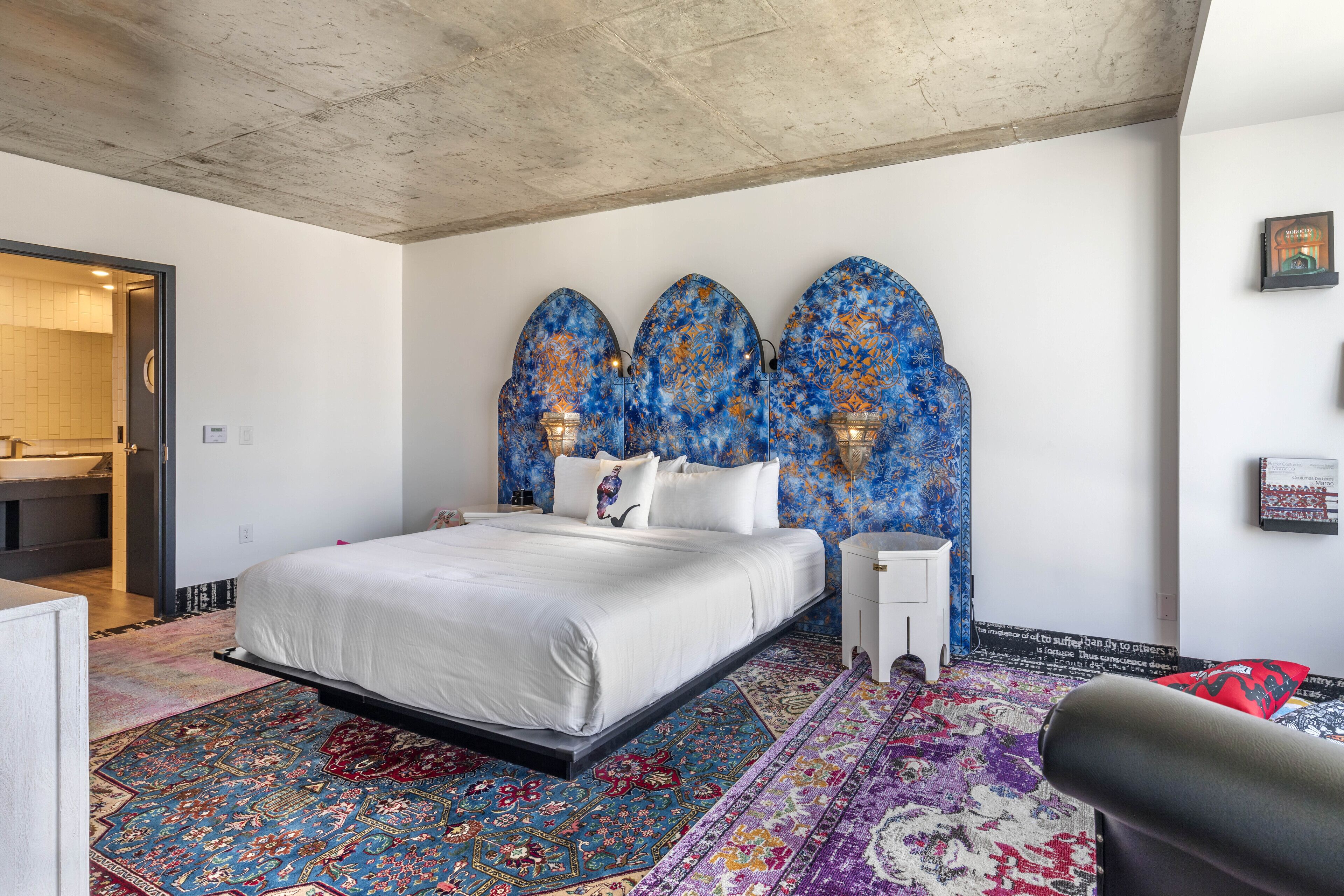A bedroom with a large bed, a patterned rug, and a unique blue and orange headboard.