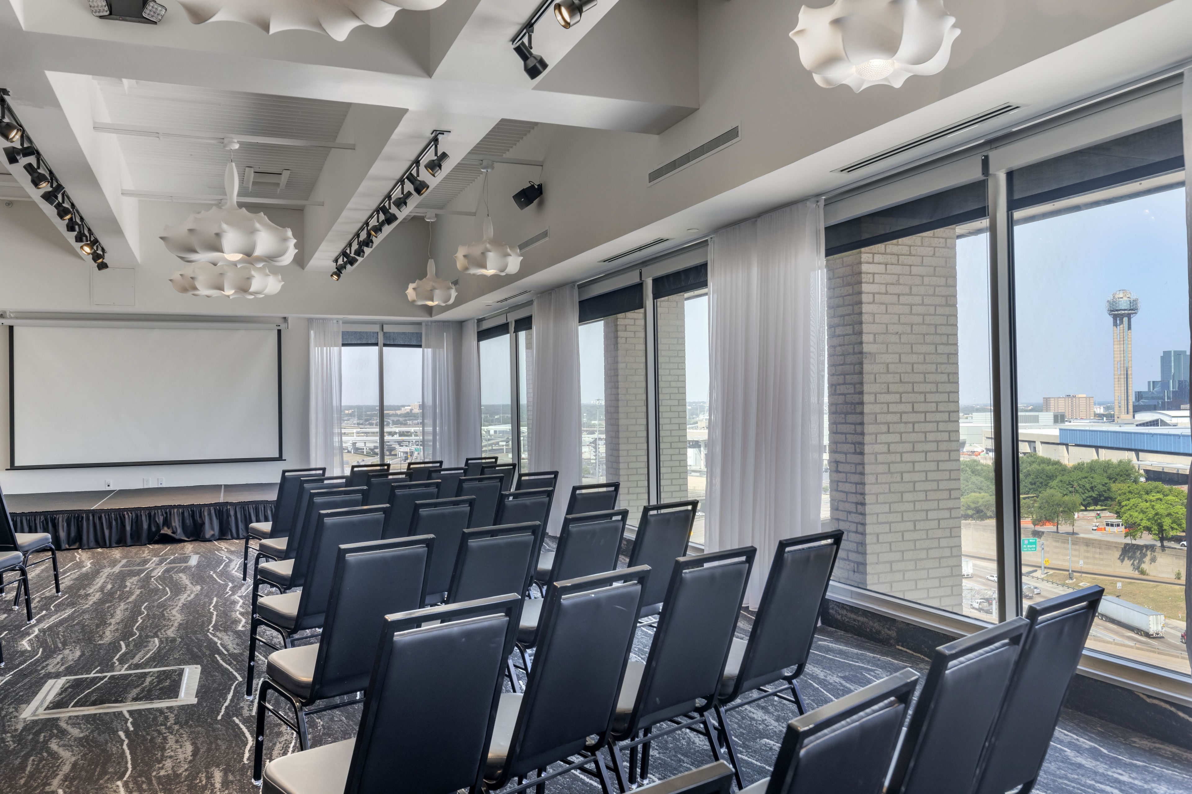 A conference room with rows of chairs, a projector screen, and large windows with a city view.