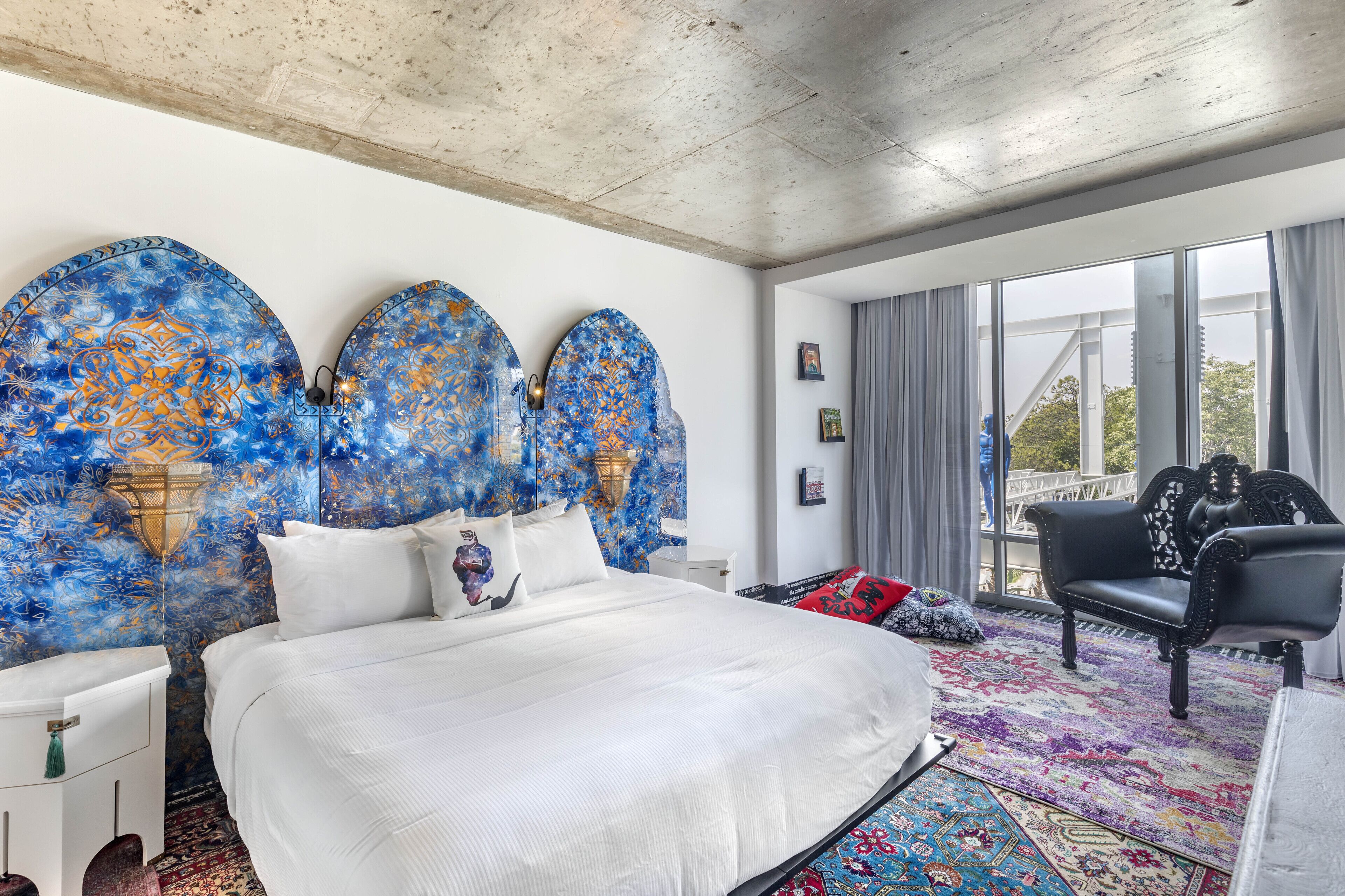 A modern hotel room with a large bed, a black leather sofa, and a colorful rug.