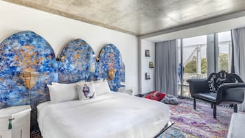 A modern hotel room with a large bed, a black leather sofa, and a colorful rug.