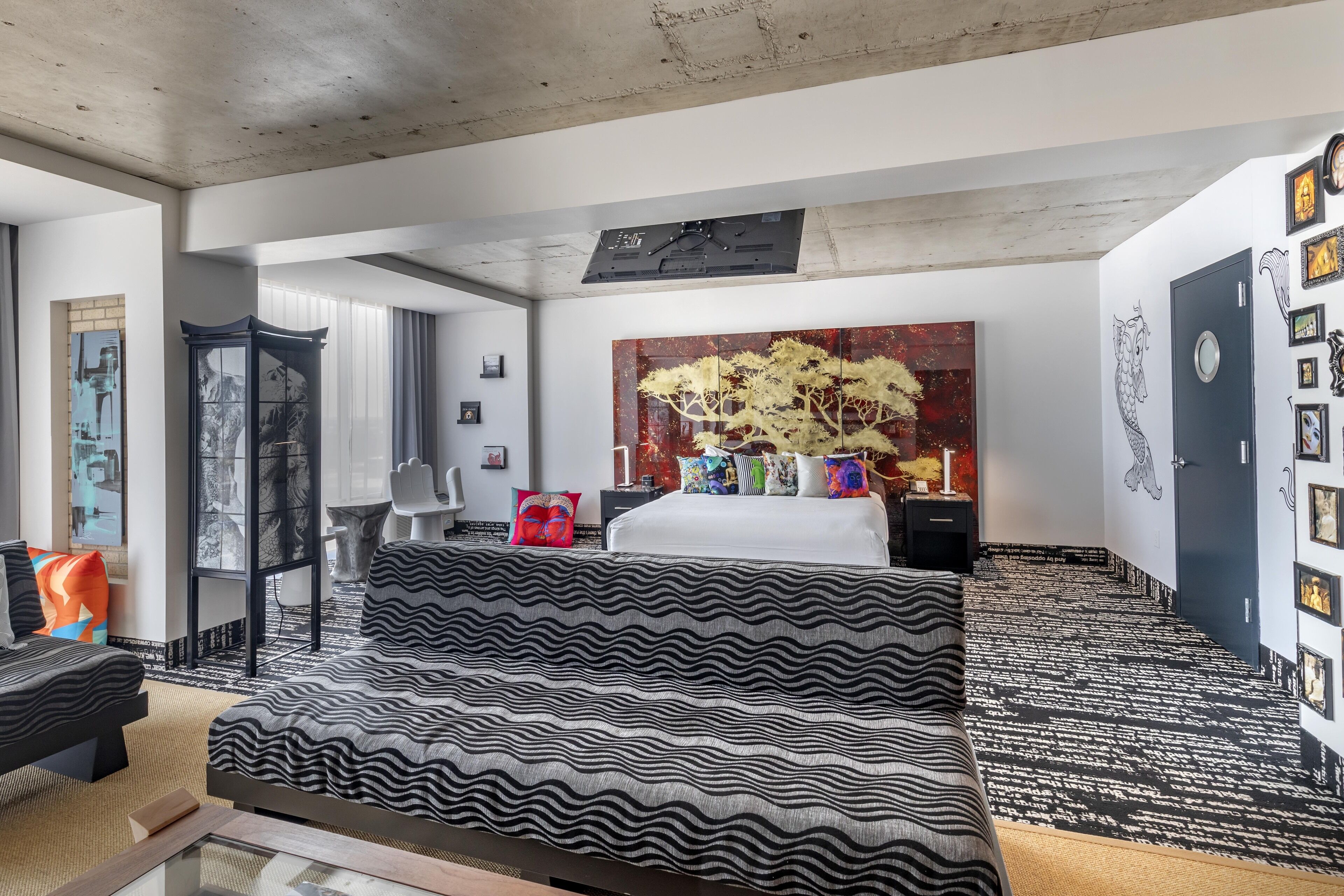 A modern hotel room with a large bed, a sofa, a desk, and a large window.