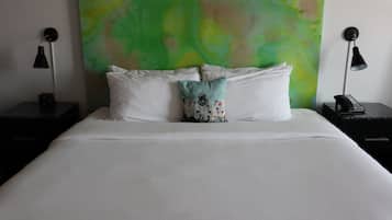 Una cama bien hecha con sábanas blancas, un cuadro abstracto verde en la pared, y dos mesitas de noche negras con lámparas y un teléfono.