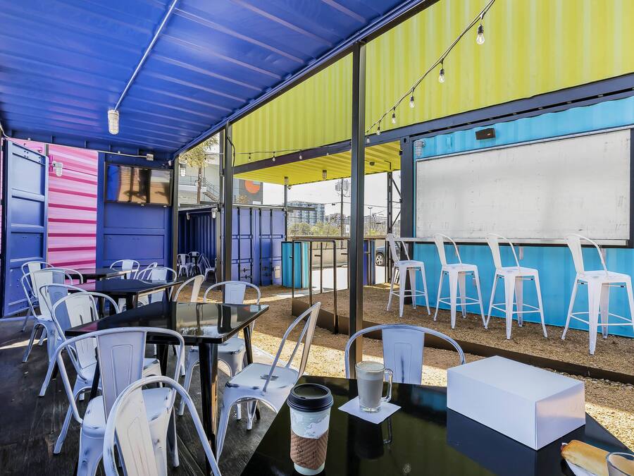 An outdoor seating area with tables and chairs, a whiteboard, and a view of the street.