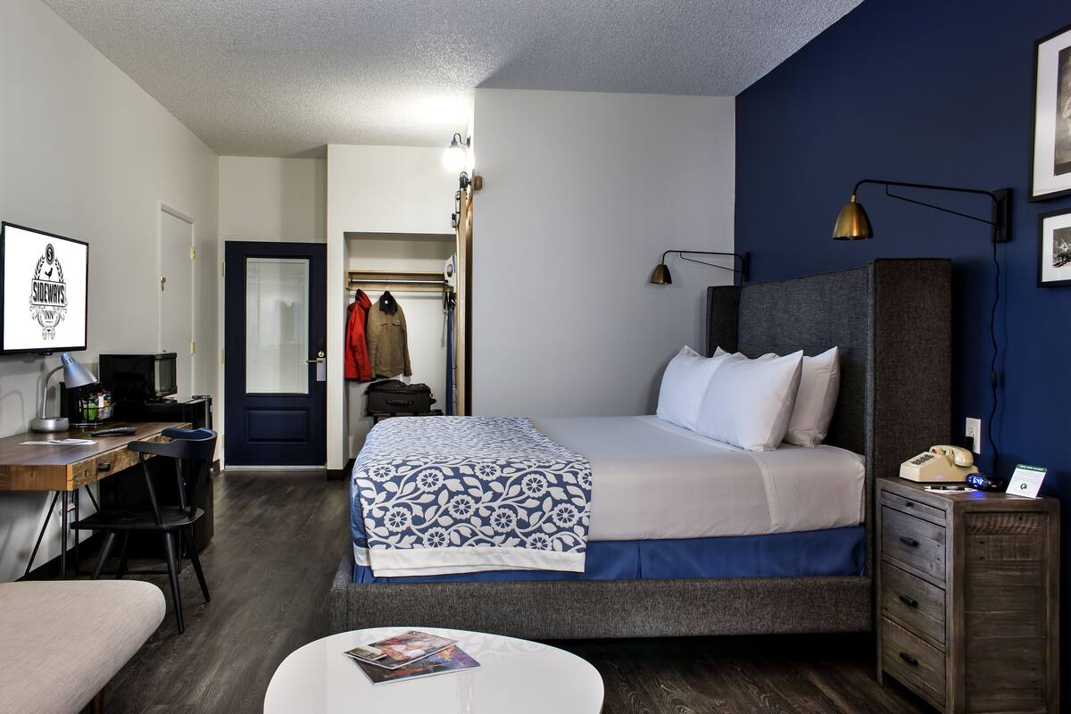 A hotel room with a bed, desk, chair, bedside table, and a wardrobe.