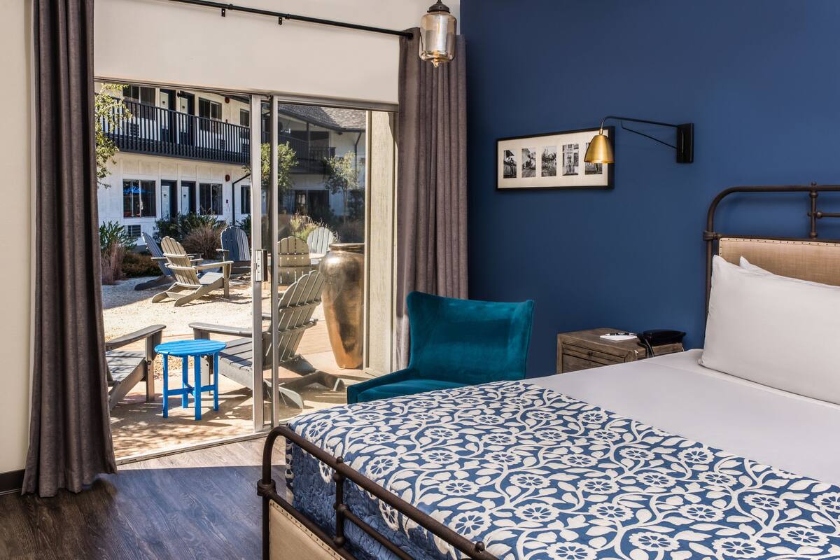 A bedroom with a bed, a chair, a nightstand, and a view of an outdoor patio with a table and chairs.