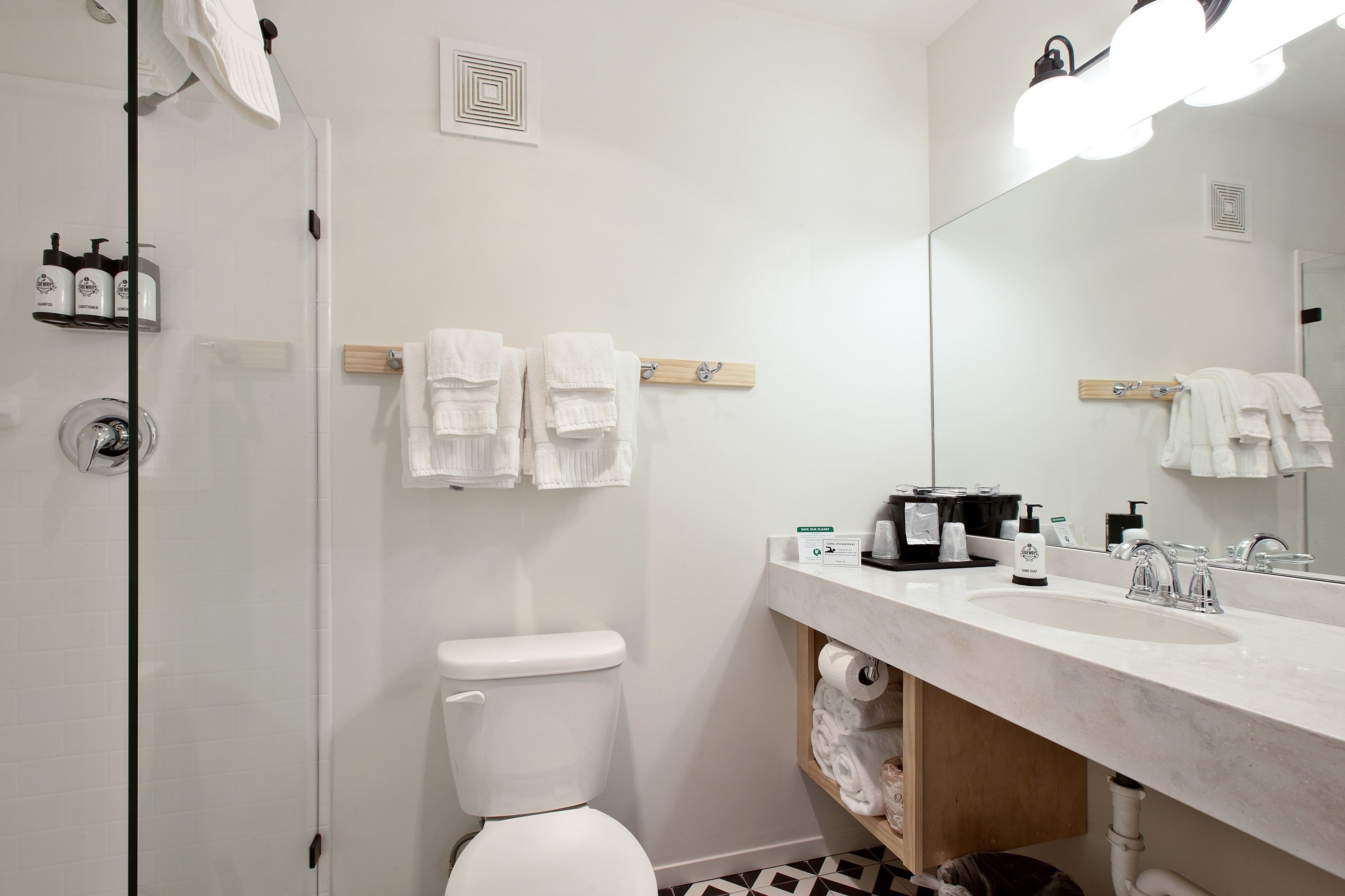 A modern bathroom with a white toilet, a glass shower enclosure, a large mirror, and a white sink with a marble countertop.