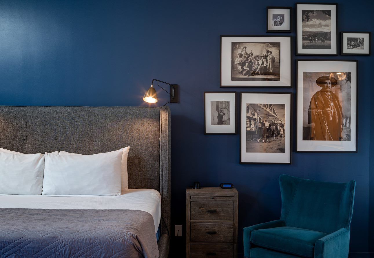 Un dormitorio con cama, mesita de noche, una silla y un cuadro en la pared con fotografías enmarcadas.