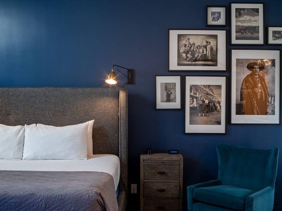Ein Schlafzimmer mit einem Bett, einem Nachttisch, einem Sessel und einer Wand mit gerahmten Bildern.
