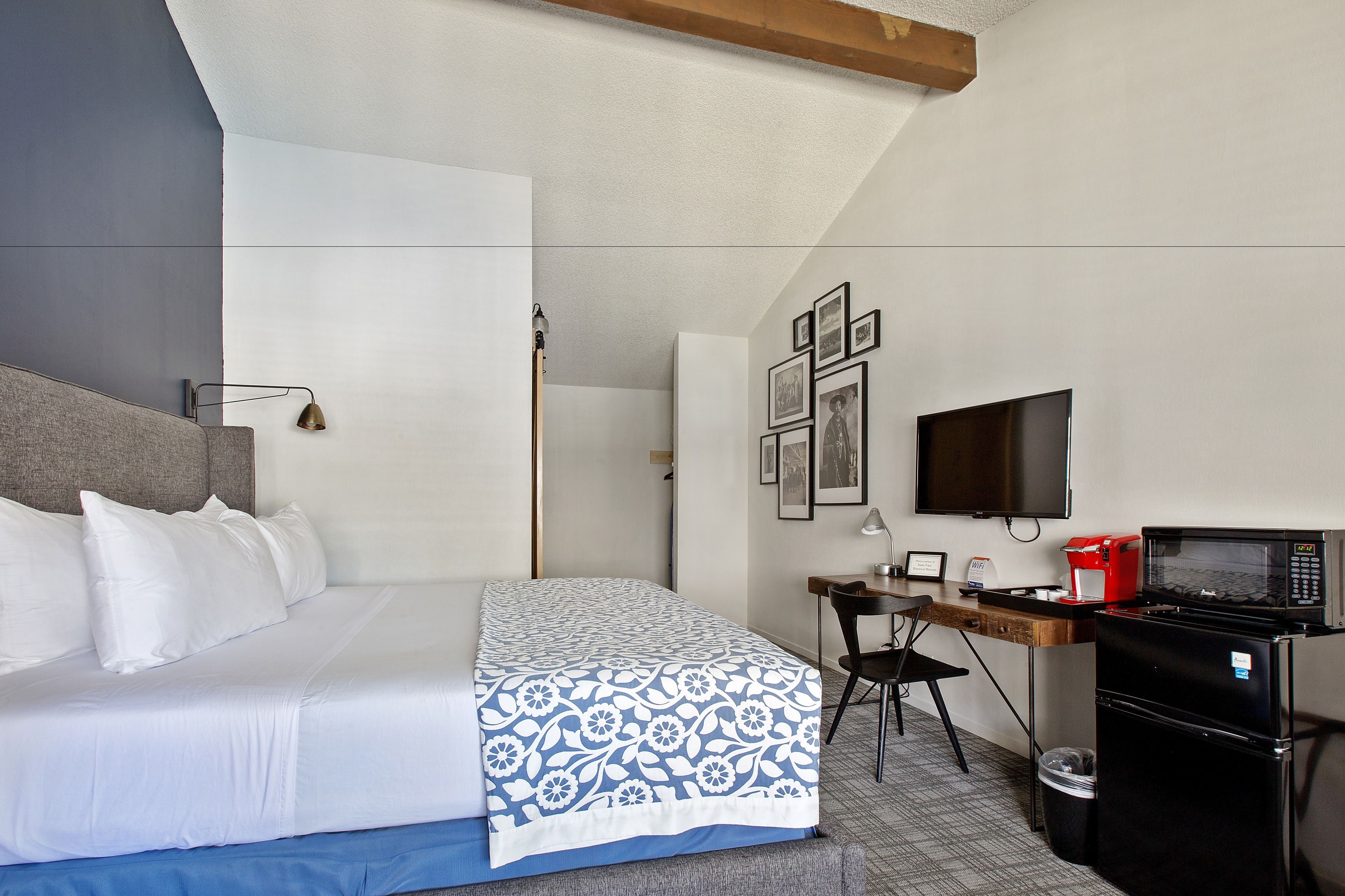 A hotel room with a bed, desk, chair, TV, and microwave.