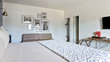 A bedroom with a large bed, a desk with a coffee maker, and several framed pictures on the wall.