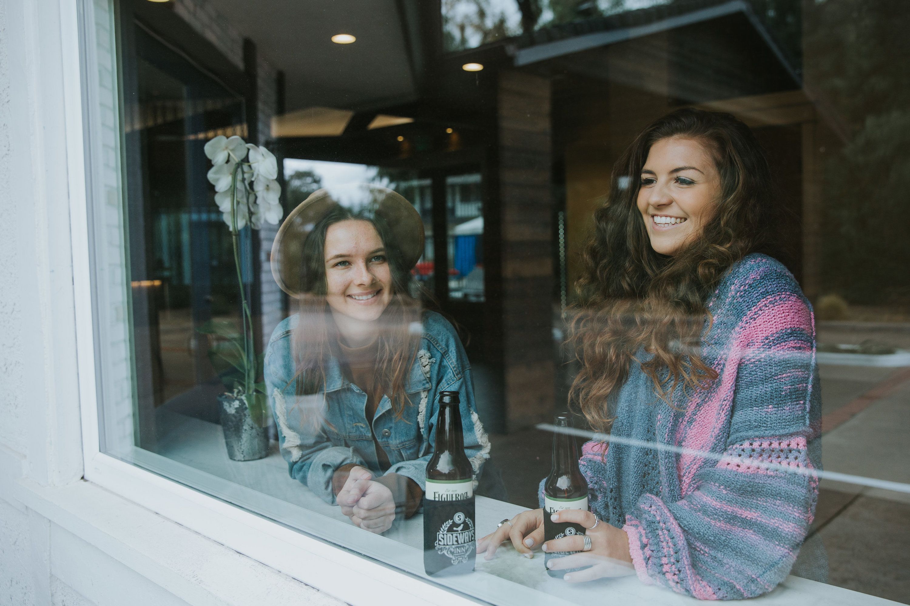 Two people sitting at a table inside a building with a window behind them.