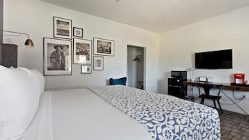 Una habitación de hotel con una cama, un escritorio con computadora, un televisor y varias fotos enmarcadas en la pared.