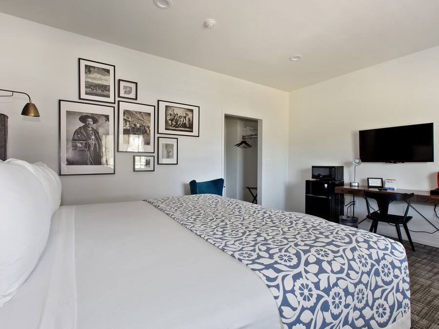 Una habitación de hotel con una cama, un escritorio con computadora, un televisor y varias fotos enmarcadas en la pared.