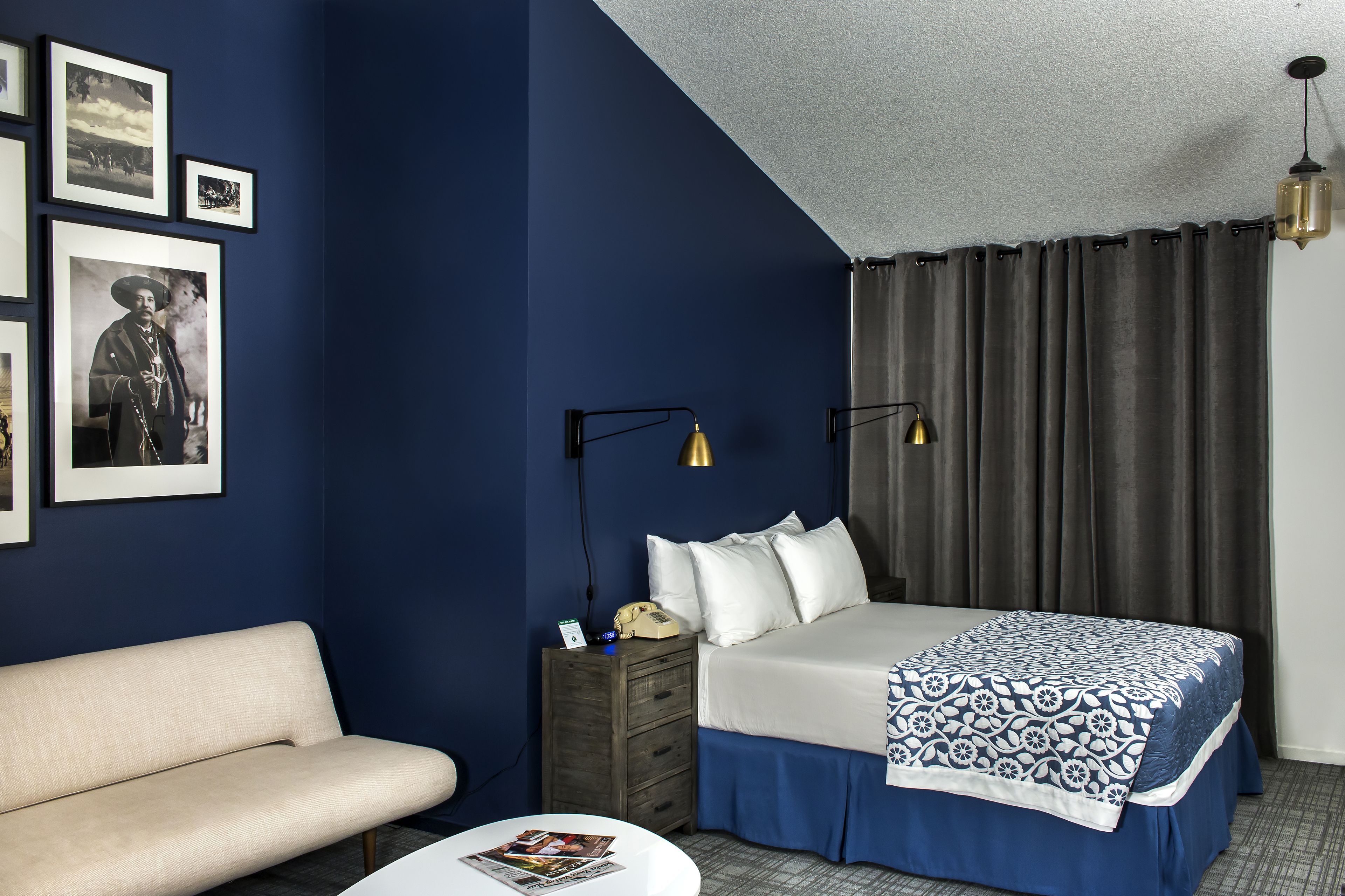 A hotel room with a bed, a bedside table with a lamp, a couch, and framed pictures on the wall.