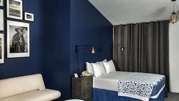Habitació d'hotel amb un llit, una taula de nit amb una làmpada, un sofà i quadres a la paret.
