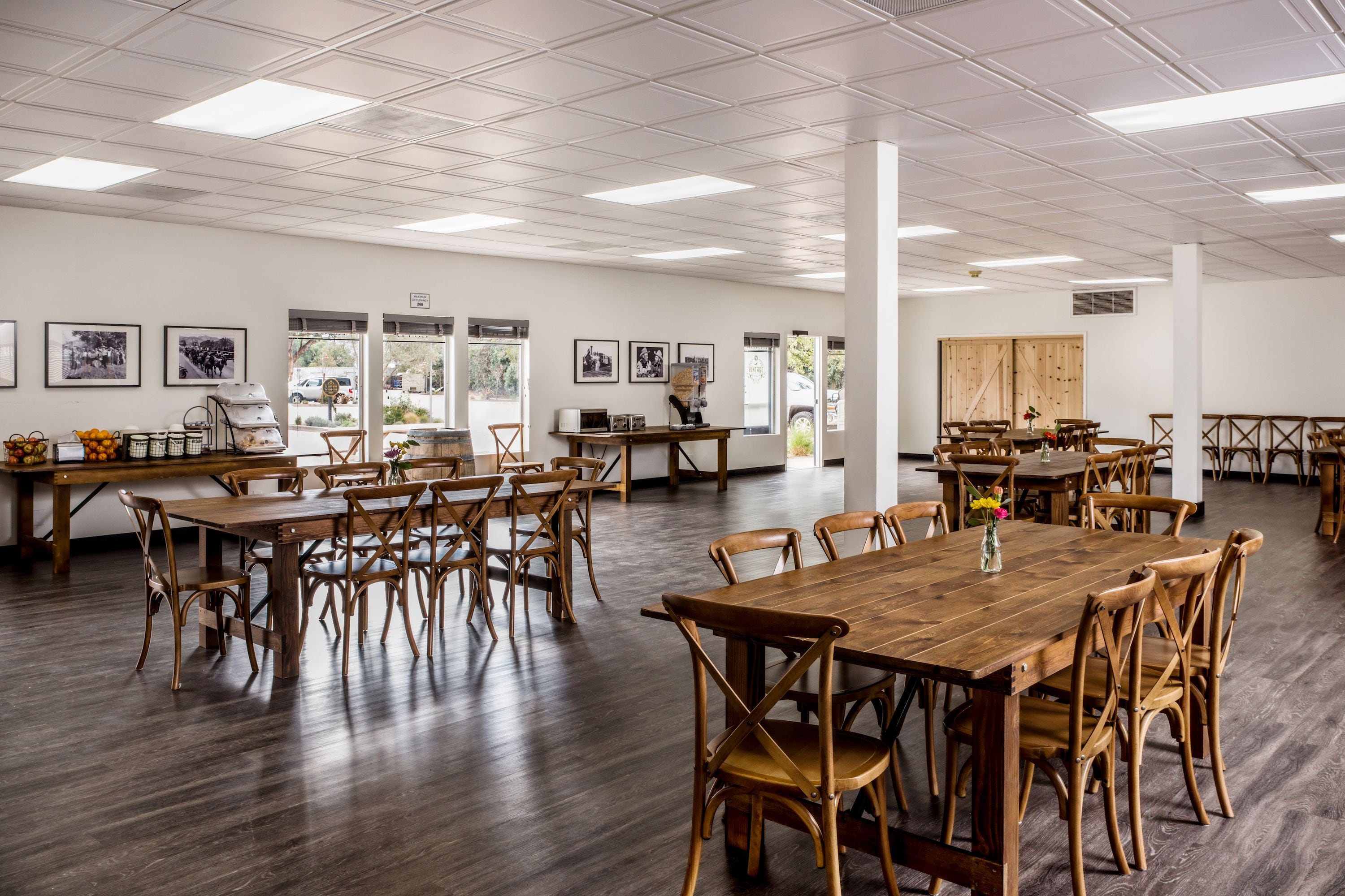 Un comedor amplio con varias mesas y sillas de madera, ventanas grandes y cuadros en las paredes.