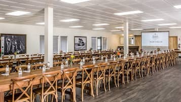 A conference room with long tables and chairs, a projector screen, and a welcome sign.
