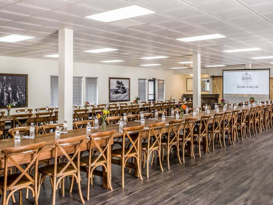 A conference room with long tables and chairs, a projector screen, and a welcome sign.