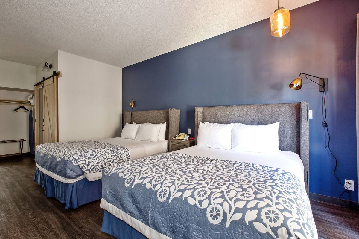 A hotel room with two beds, a wardrobe, a desk, and a lamp.