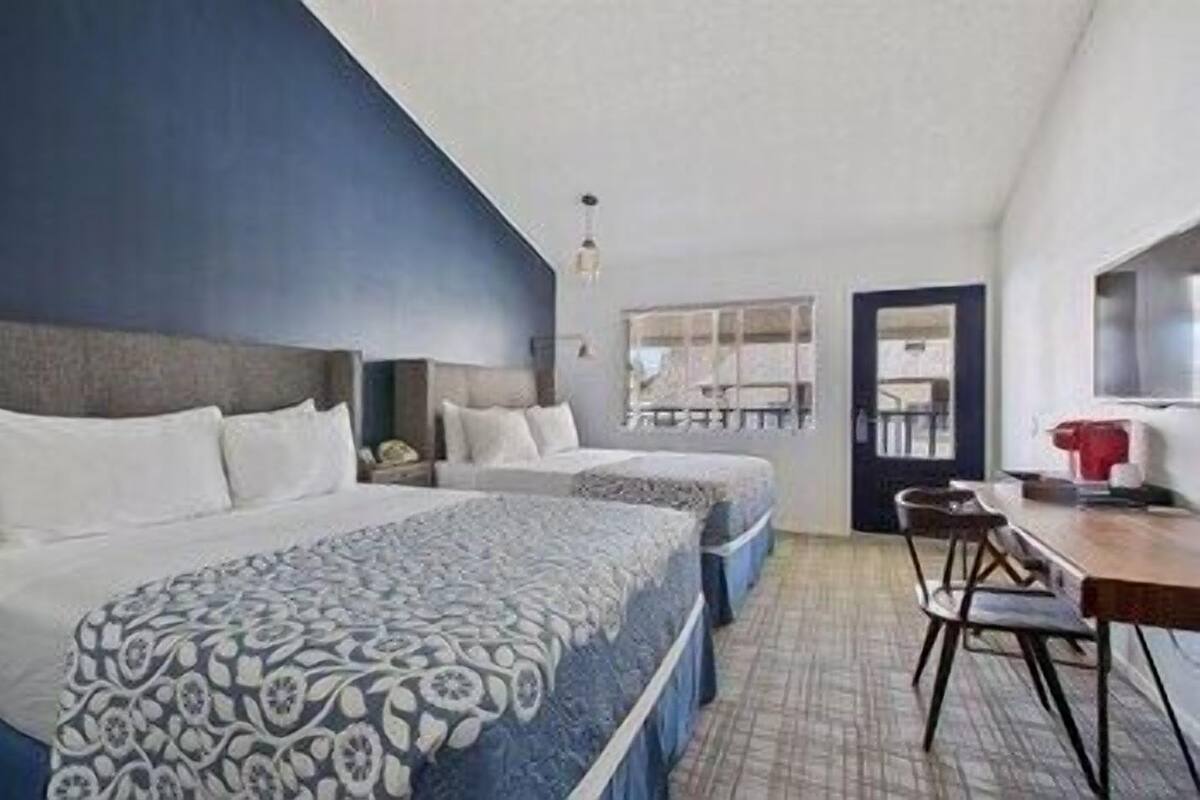 A hotel room with two beds, a desk, and a chair.