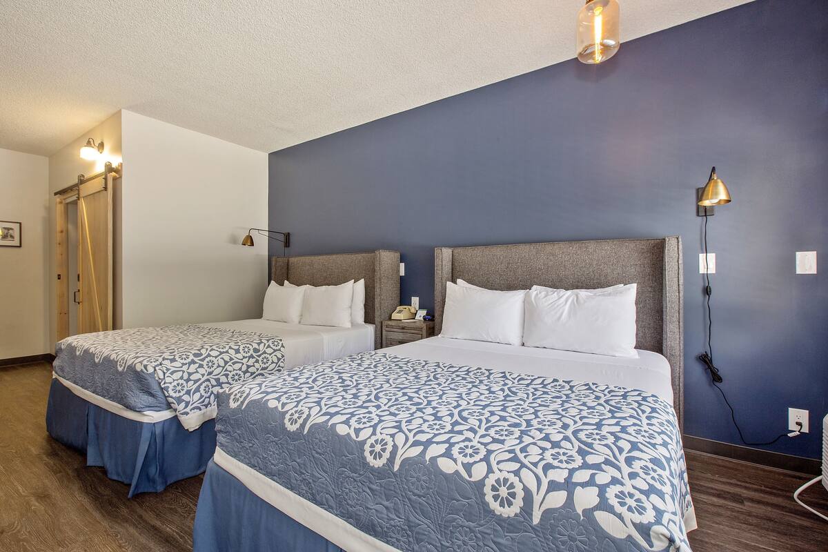 A hotel room with two beds, each with a blue floral bedspread, wooden headboards, and bedside lamps.