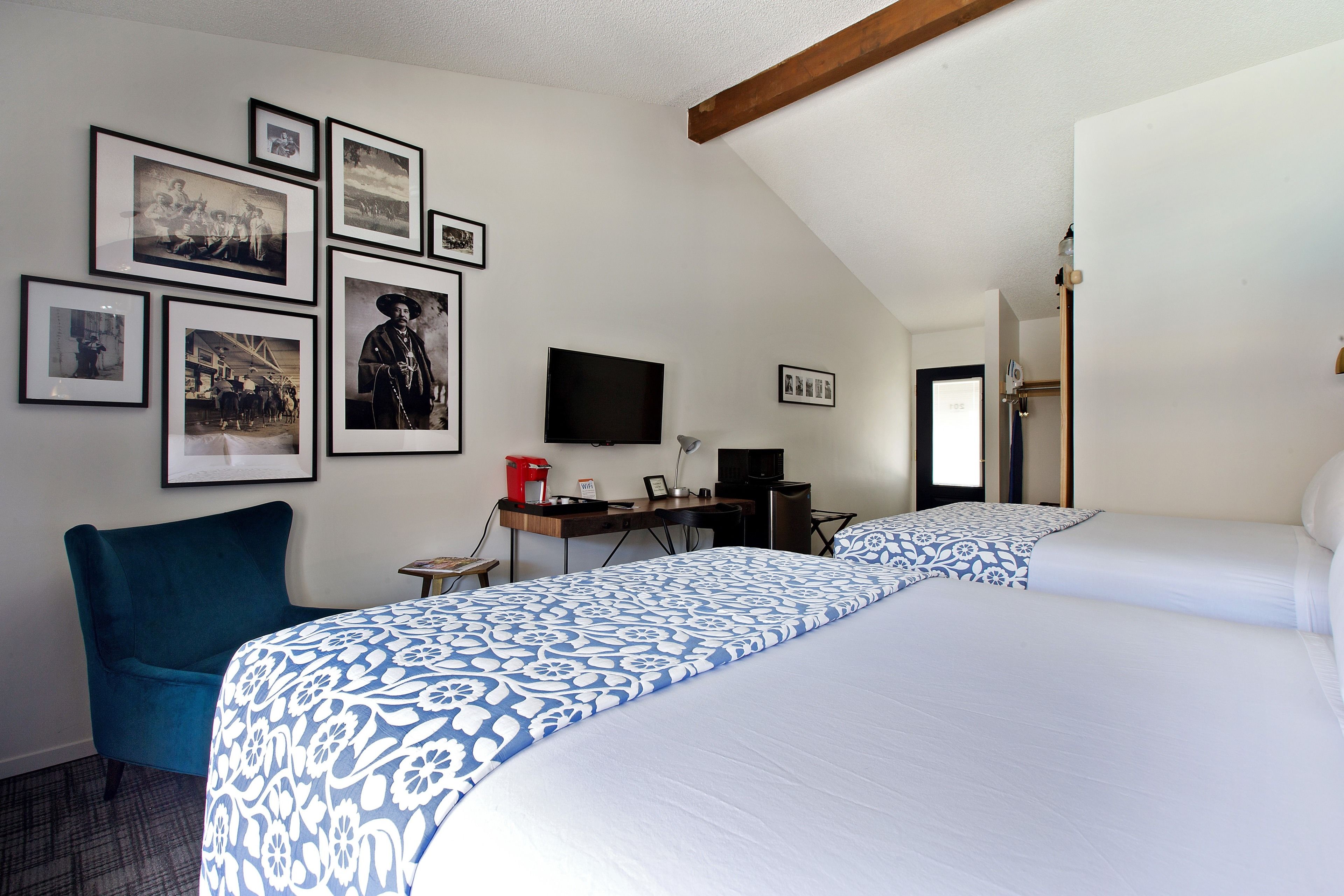 A hotel room with two beds, a desk with a computer, a TV, and framed pictures on the wall.