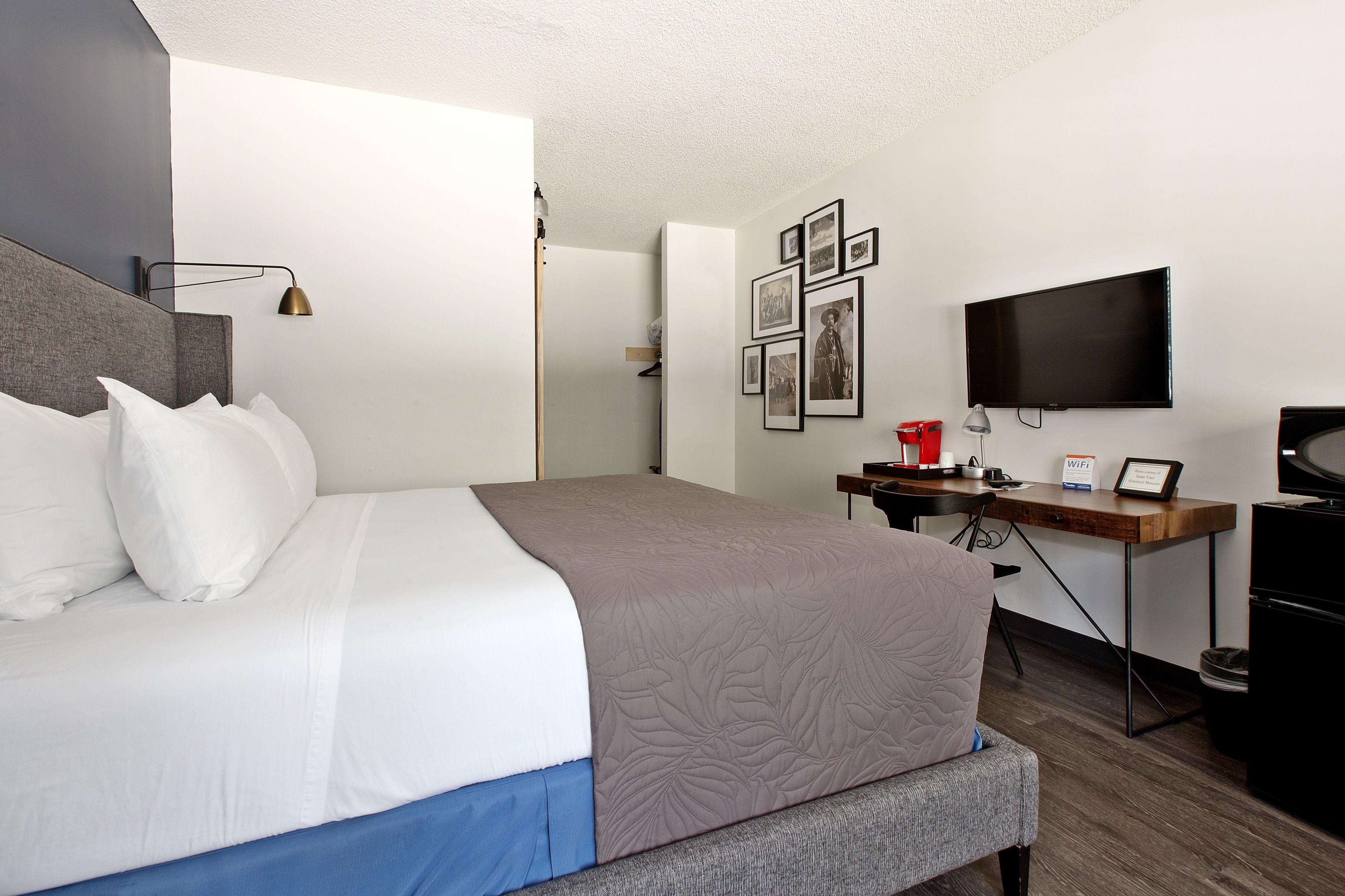 A hotel room with a bed, a desk, a TV, and framed pictures on the wall.