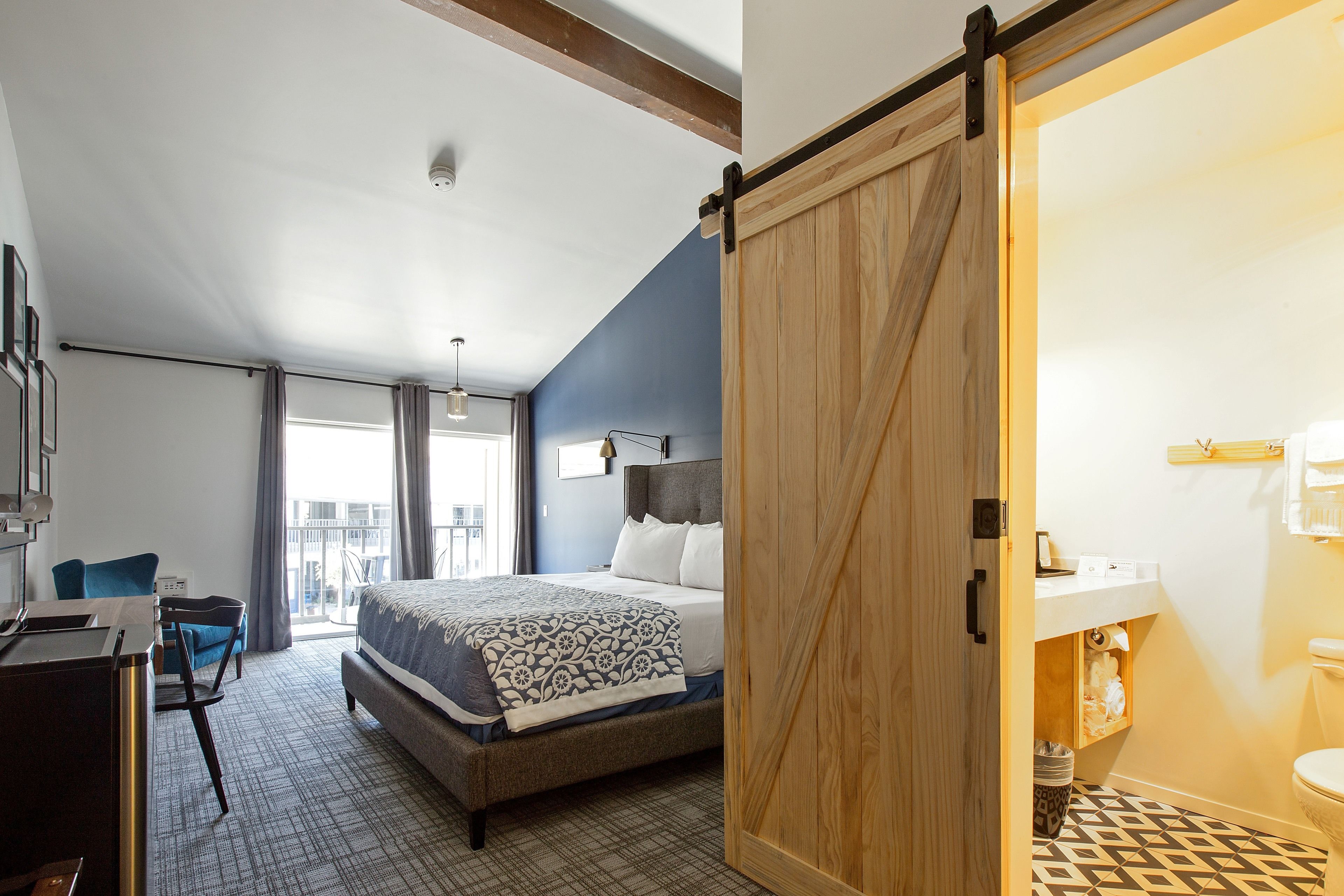 A hotel room with a bed, a desk, a chair, a bathroom, and a view of the outside.