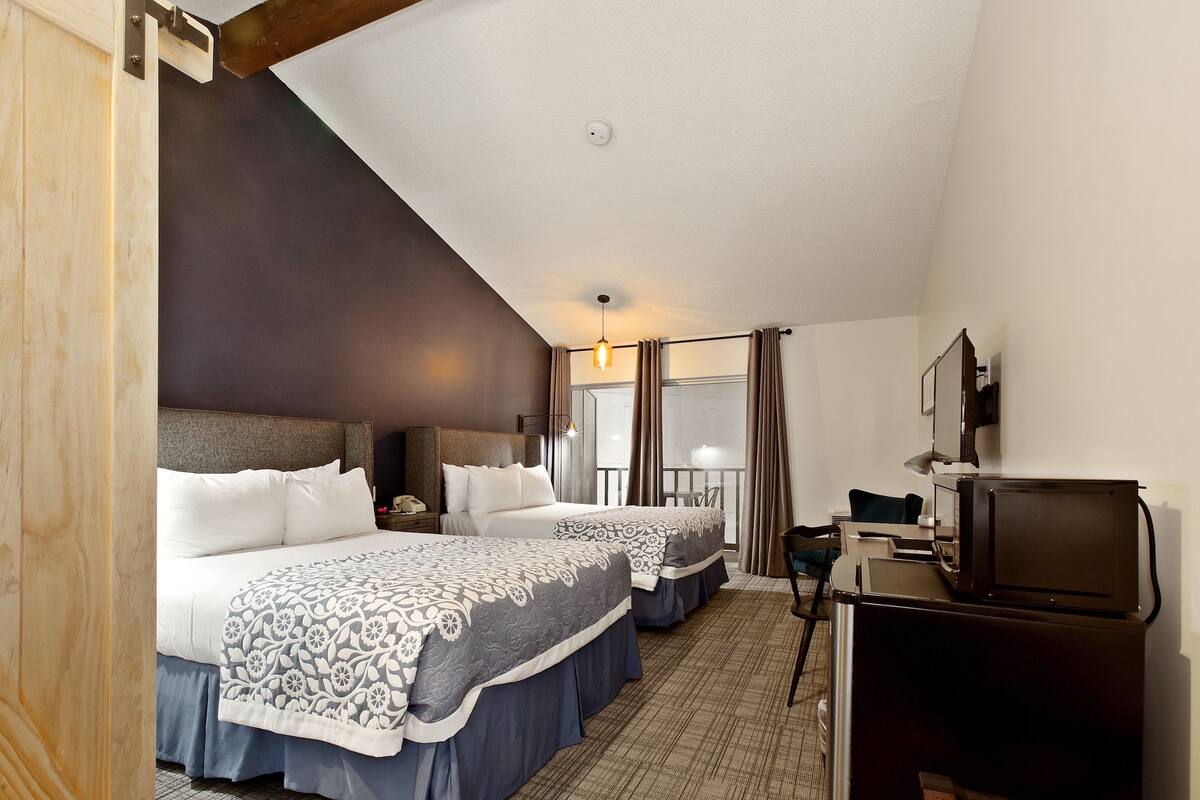 A hotel room with two beds, a desk with a computer, a TV, and a window with curtains.