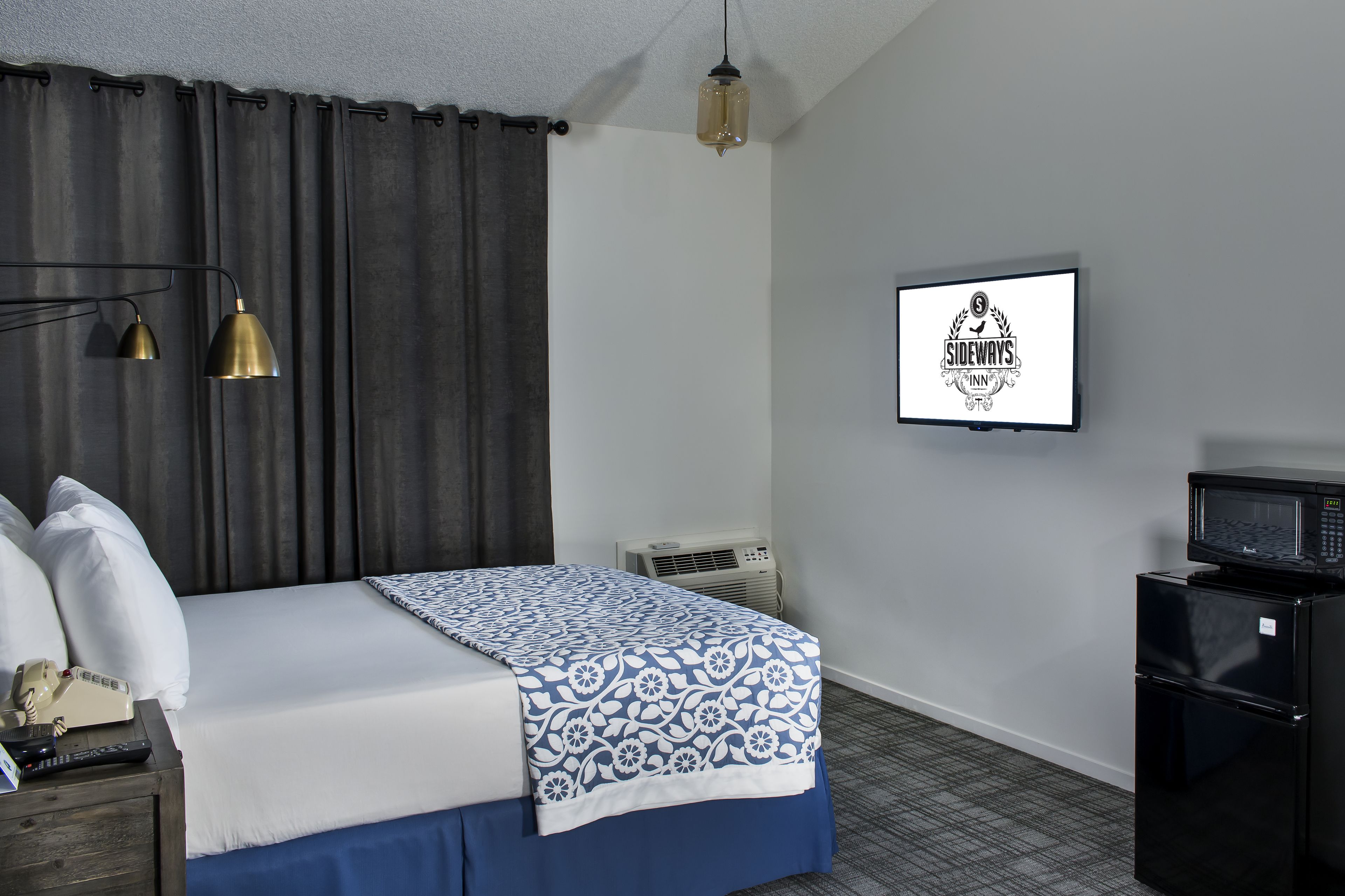 Quarto de hotel com cama, luminária de cabeceira, ar condicionado e micro-ondas.