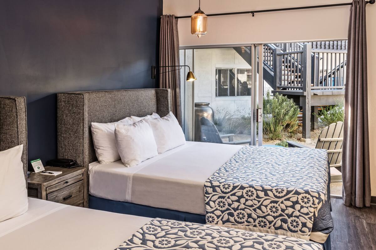 A bedroom with a large bed, a nightstand, a window with a view of a balcony and stairs, and a hanging light fixture.