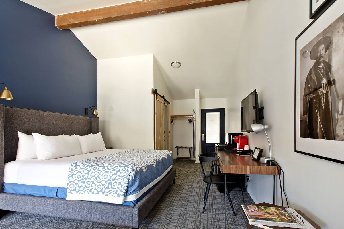 A hotel room with a bed, desk, chair, and a framed picture on the wall.