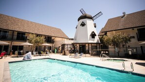 A swimming pool area with lounge chairs and umbrellas, a windmill, and a building with a tiled roof.