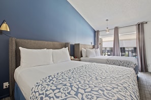 A hotel room with two beds, a large window with curtains, and a ceiling light.