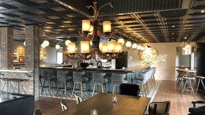 A modern bar area with a wooden bar counter, multiple bar stools, and a unique antler chandelier.