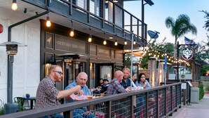 A restaurant with outdoor seating, a sign indicating it serves cocktails, beer, and wine, and a decorative shield emblem.
