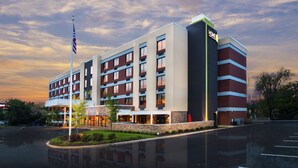 A multi-story hotel with a modern design, featuring a prominent 'HOME' sign, a flagpole with an American flag, and a reflection in the water.