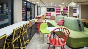 A modern lounge area with a green sofa, red and yellow chairs, a white table, and a TV mounted on the wall.