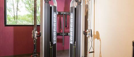Une salle de sport équipée de machines de musculation, d’un banc et d’une fenêtre donnant sur des arbres.