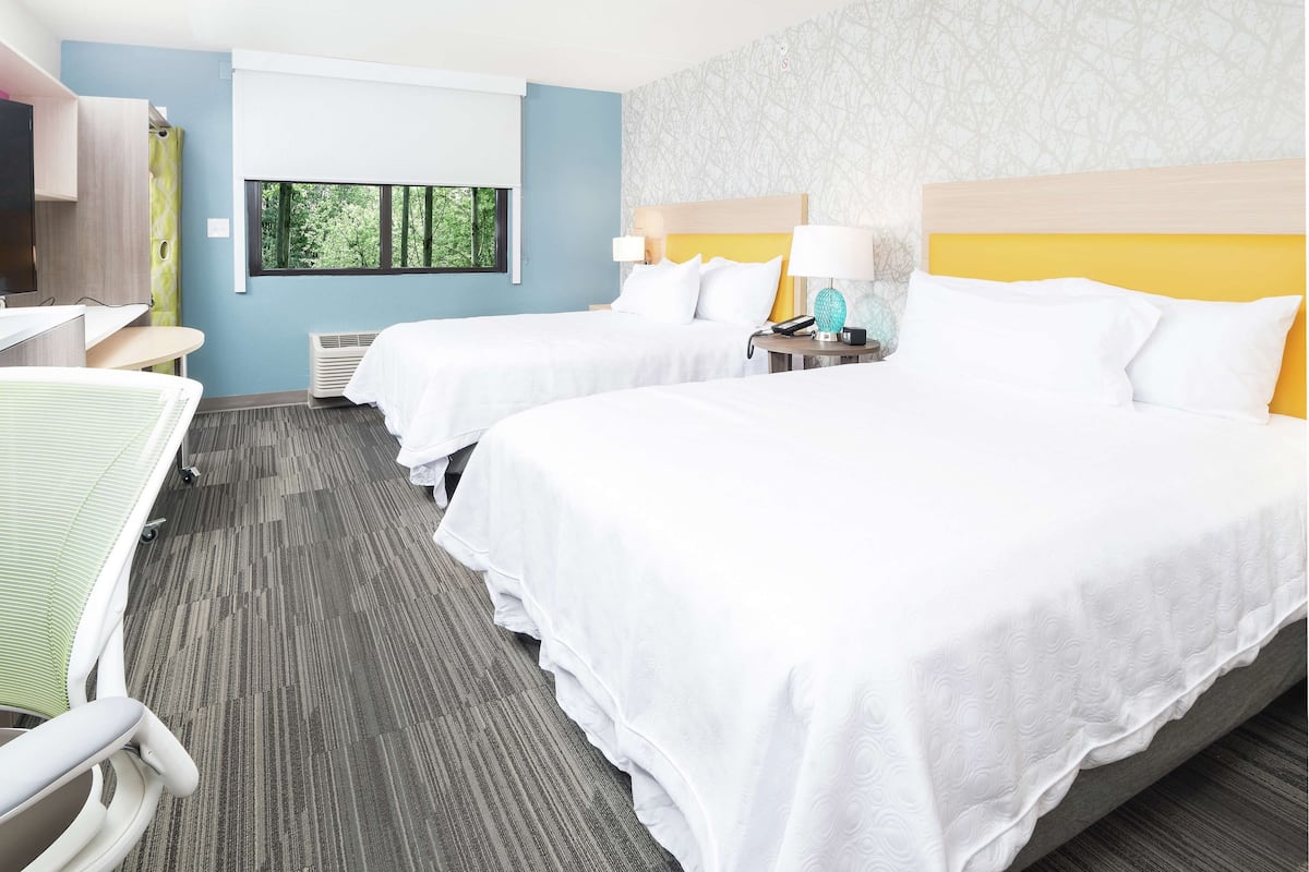 A hotel room with two beds, a desk, a chair, a window, and a shower area.