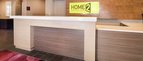 A hotel reception area with a reception desk, a 'HOME 2' sign, a 'HOME' sign, and a 'EXIT' sign.