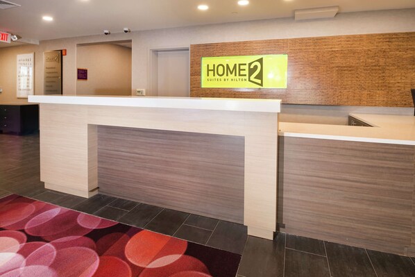 A hotel reception area with a reception desk, a 'HOME 2' sign, a 'HOME' sign, and a 'EXIT' sign. - Home2 Suites by Hilton King of Prussia/Valley Forge, PA (King of Prussia)