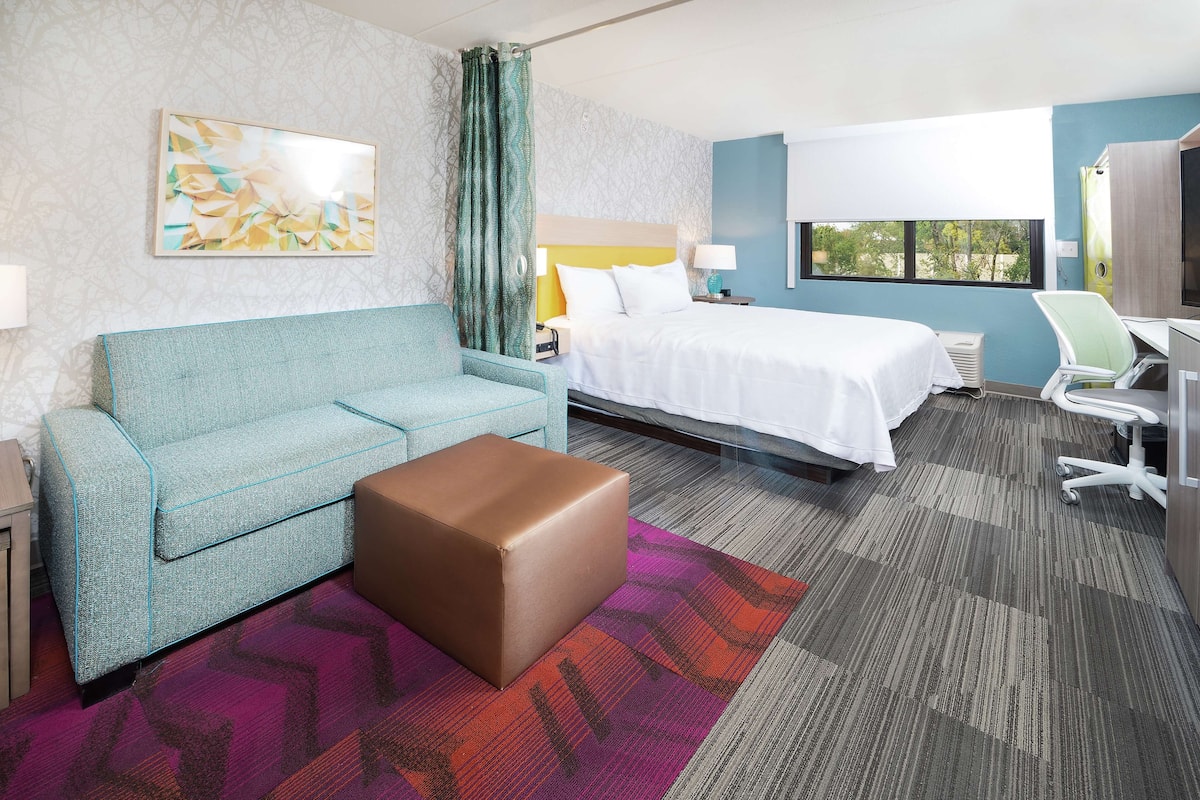 A hotel room with a bed, a sofa, a desk, and a chair.