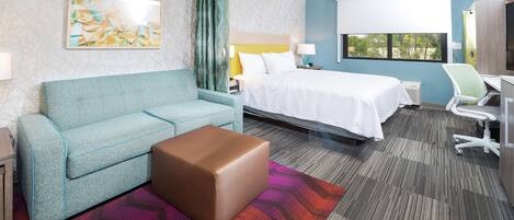A hotel room with a bed, a sofa, a desk, and a chair.