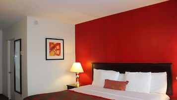 A hotel room with a bed, a nightstand with a lamp, a door, and a framed picture on the wall.